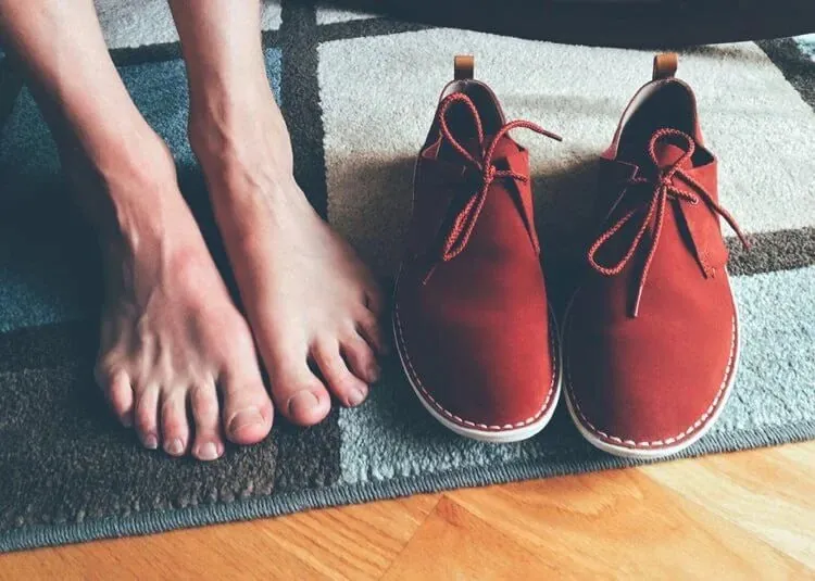 Bare feet on a rug beside a pair of red lace-up shoes